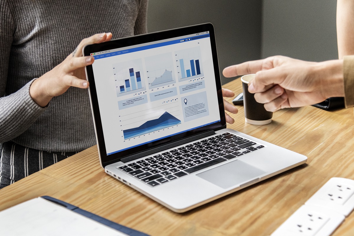 Notebook sobre mesa de madeira com duas pessoas analisando gráficos no mesmo em escritório