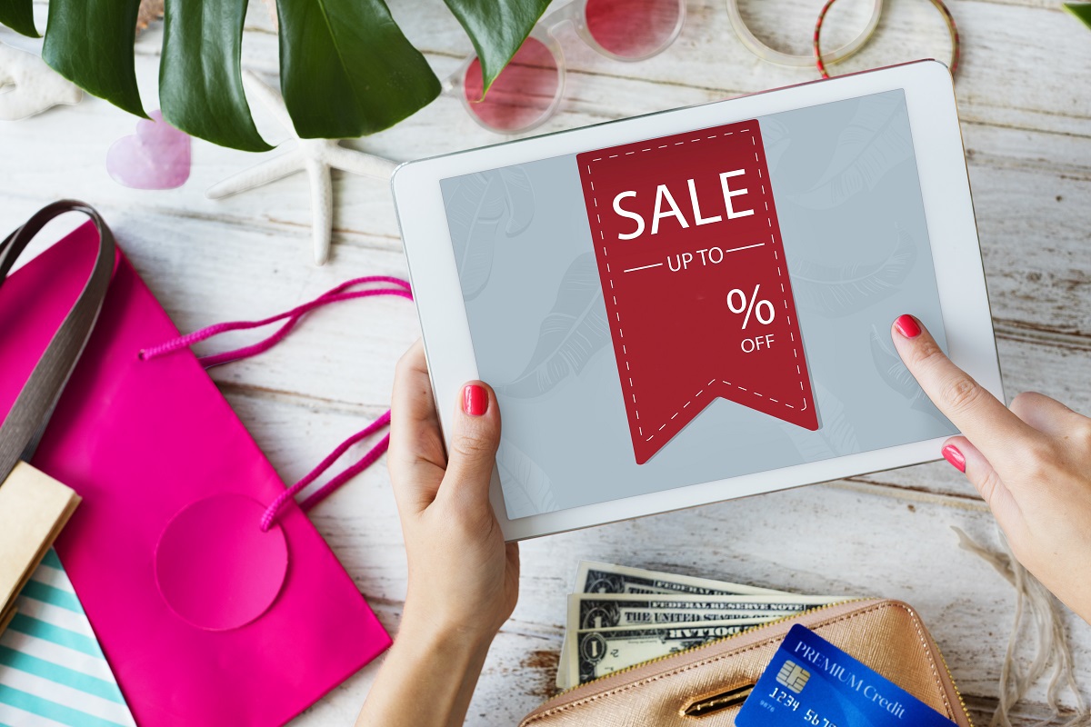 Tablet: CTA para e-commerce Mulher com unhas pintadas de rosa em tom forte segurando tablet acima de mesa de madeira que suporta objetos pessoais femininos