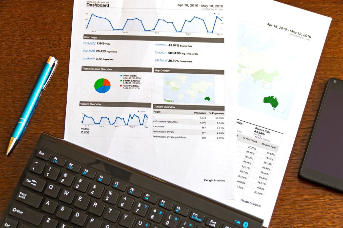 Dados impressos: ciência do comportamento Dados impressos em folhas de papel a4 sobre mesa de madeira com caneta azul ao lado esquerdo e celular ao lado direito com parte dos papéis embaixo de teclado de computador de mesa