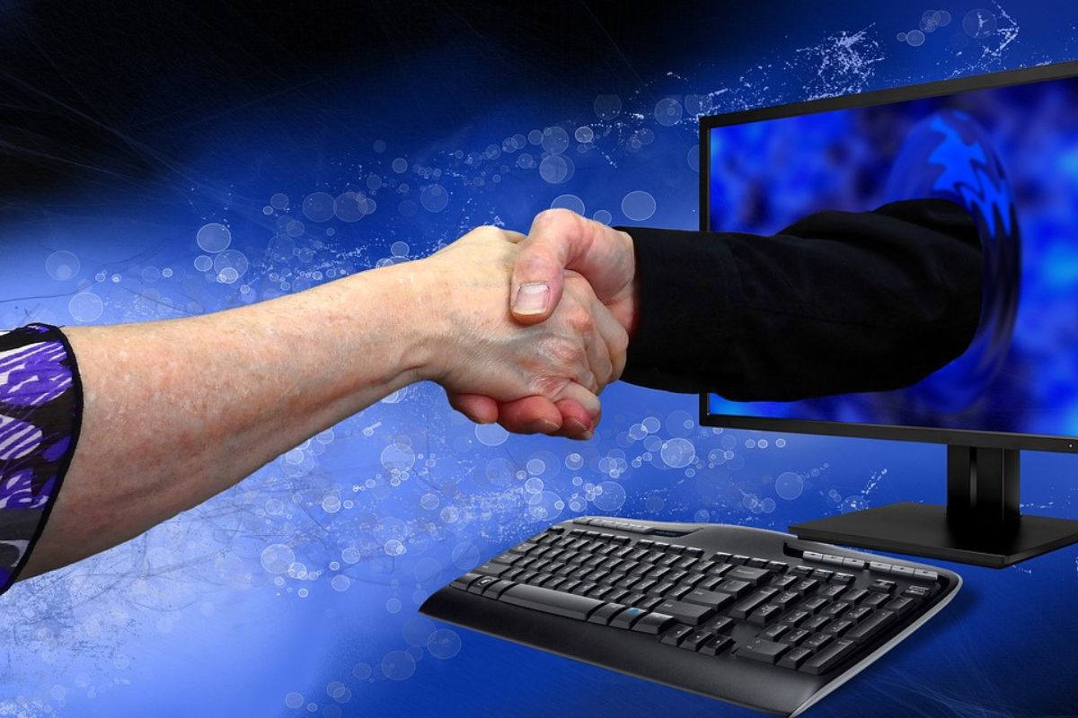 Acordo: ciência do comportamento Homem aperta mão de pessoa em montagem onde uma das mãos sai de tela de monitor de computador