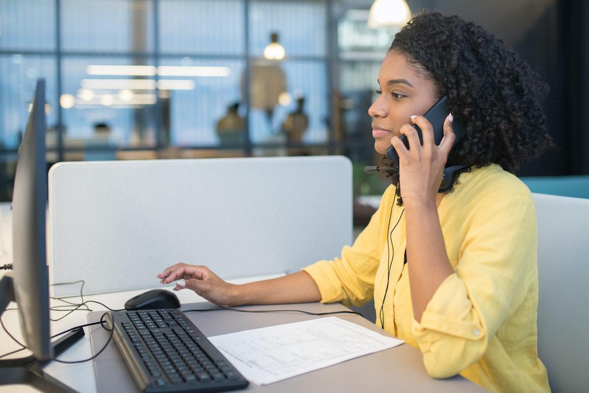 Mulher usando telefone em local de trabalho diante de mesa com computador