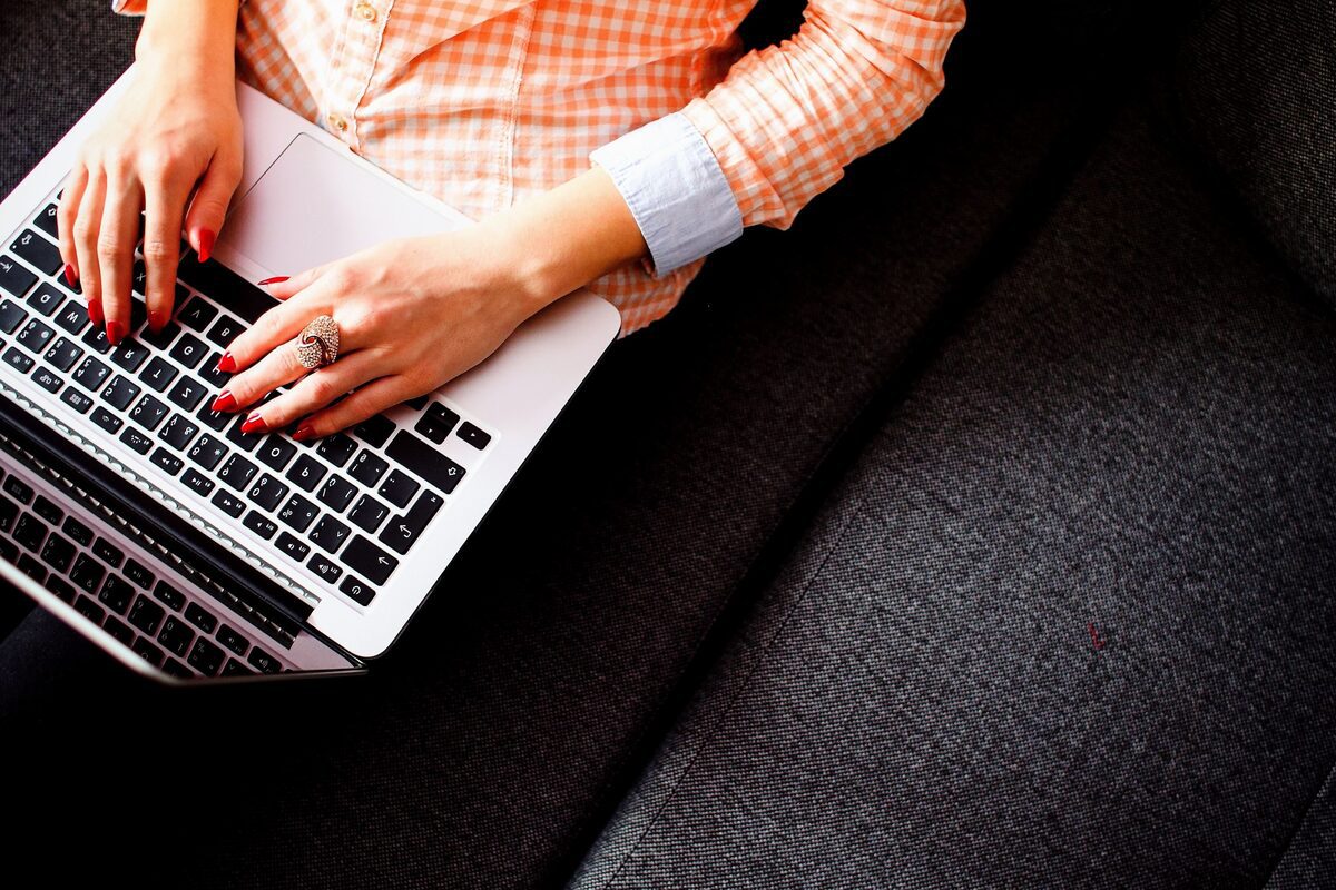 Mulher com notebook: como estimular criatividade Mulher sentada em local análogo à sofá com notebook cinza no colo