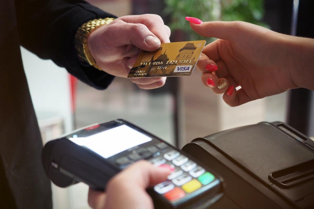 Homem entregando cartão de crédito dourado à mulher que segura pinpad para concluir transação