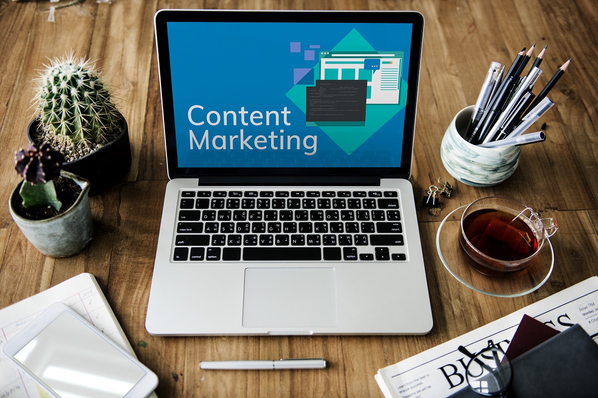 Notebook sobre mesa de madeira com objetos ao redor e montagem com frase Content Marketing na tela