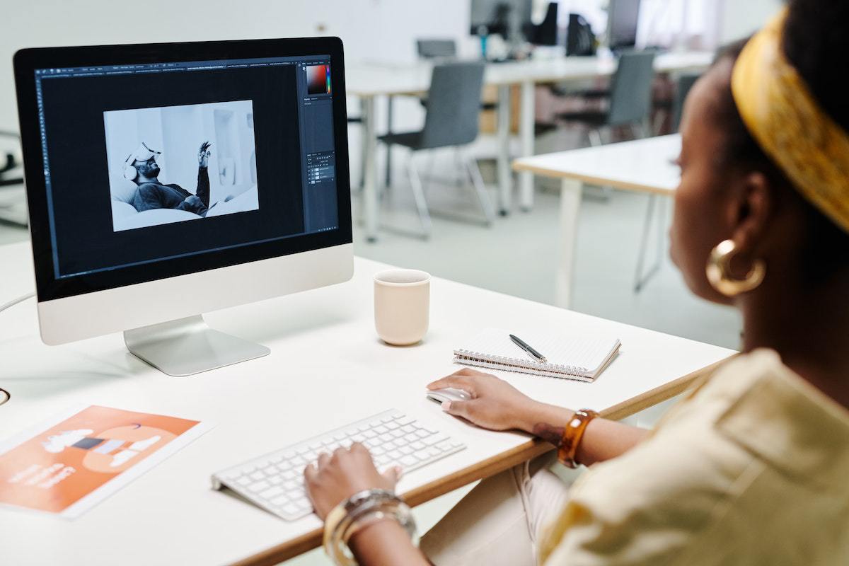 Mulher sentada diante de mesa branca em escritório editando imagens em computador de mesma cor