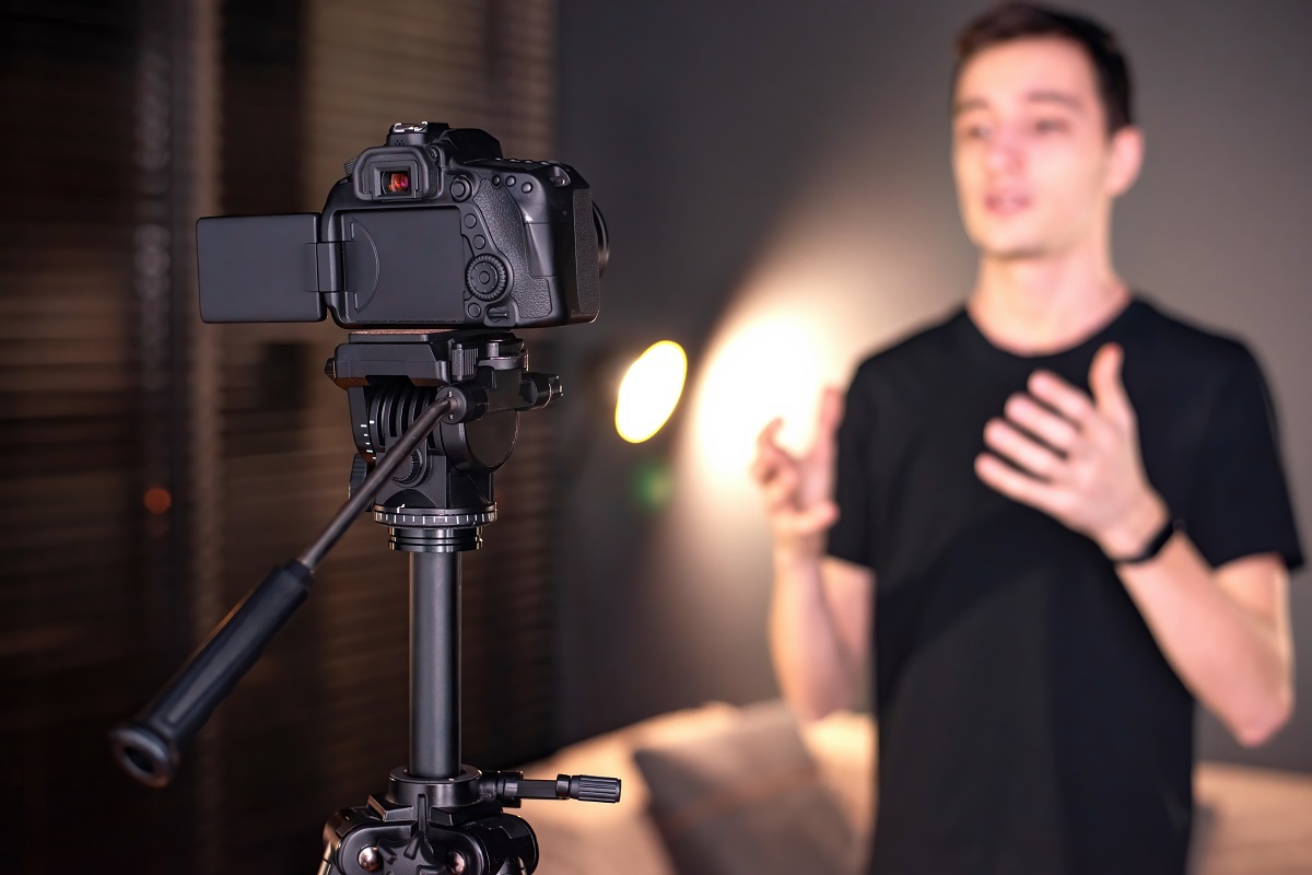 Câmera em pedestal posicionada diante de jovem usando roupa preta gesticulando e gravando vídeo