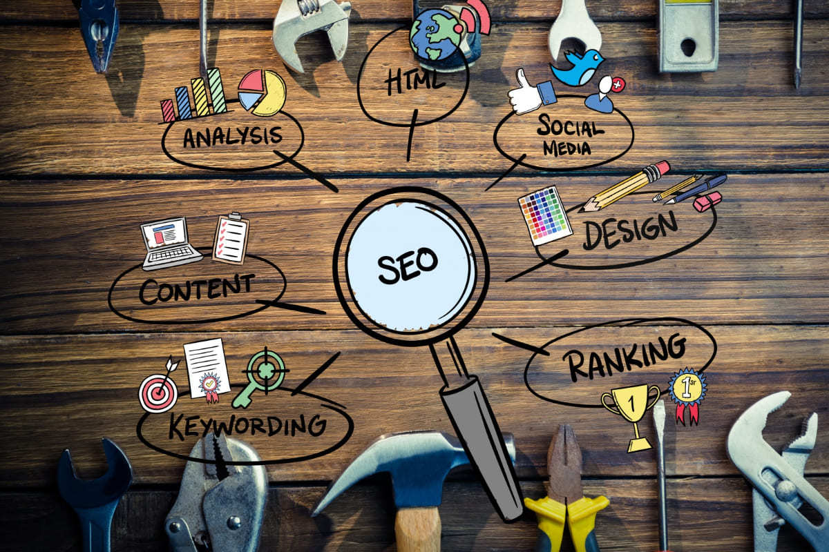 Símbolos web: Extensões para SEO do Google Chrome Montagem com símbolos que representam temas do SEO sobre mesa de madeira, além de lupa no centro com foco na sigla