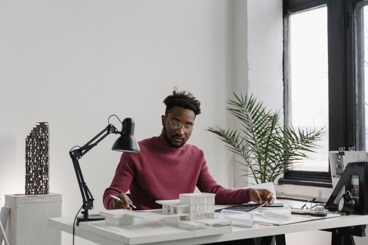 Homem sentado diante de mesa em escritório analisando dados em papéis e aparelhos