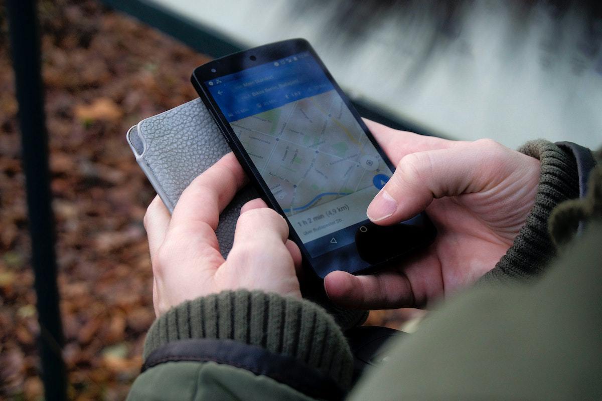 Pessoa segurando case e celular nas mãos e procurando endereço no Google Maps