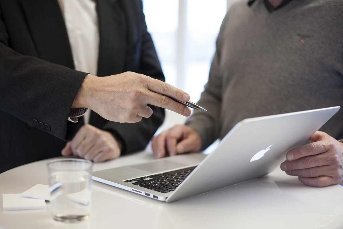 Notebook: Marketing baseado em contas Dois homens de pé diante de mesa redonda branca analisando algo em notebook apple