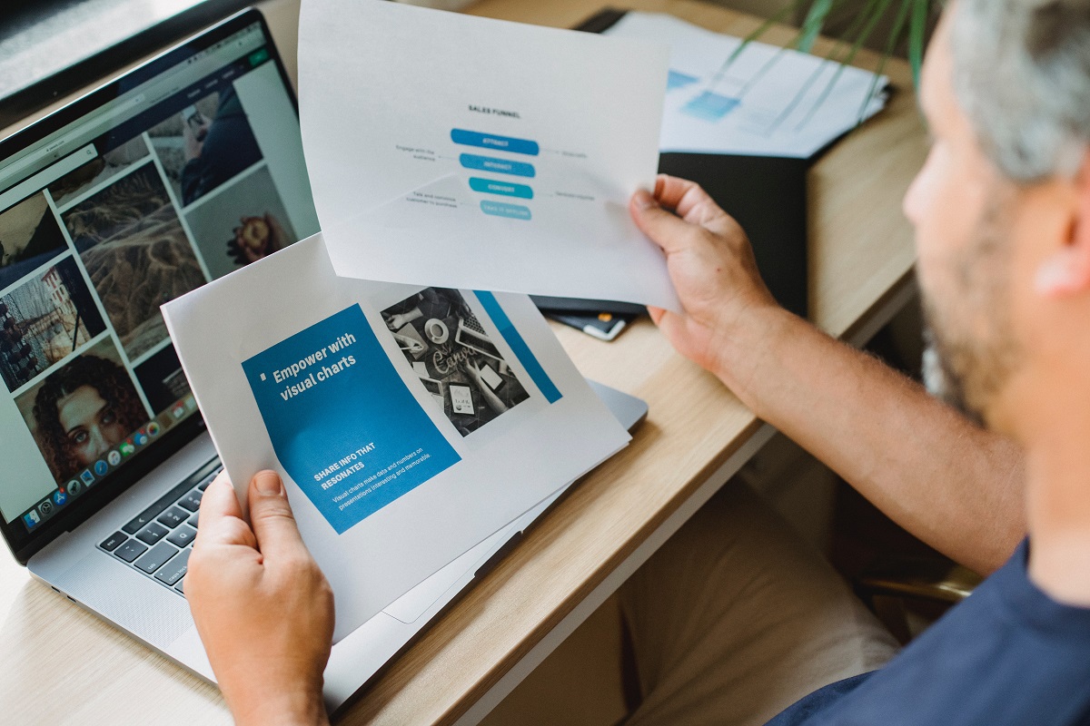 Gráficos: Marketing de conteúdo e design Homem sentado diante de mesa usando notebook e analisando gráficos impressos em folhas a4