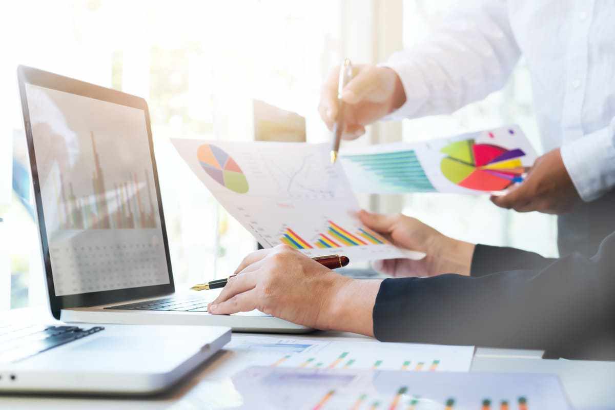 Escritório: Marketing digital para e-commerce Duas pessoas analisando dados em notebook e gráficos impressos em folhas a4 em escritório