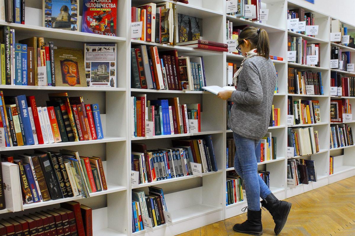 Mulher diante de estante de livros em livraria ou biblioteca