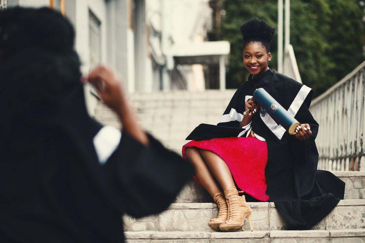 Mulher sentada em escadaria com roupa de formatura segurando diploma