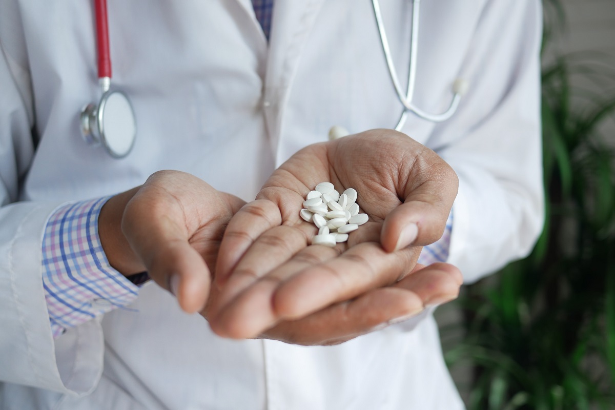 Comprimidos: marketing farmacêutico Pessoa com mãos juntas, uma sobre a outra, de palmas para cima, com jaleco e estetoscópio ao redor do pescoço, enquanto segura comprimidos brancos e pequenos em montante no meio da palma da mão