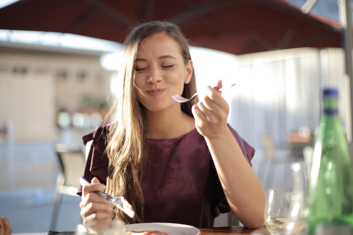 Mulher com ar sorridente comendo algo em ambiente externo de restaurante