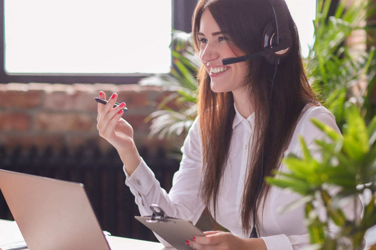 Atendimento: Marketing one to one Mulher sentada diante de mesa com notebook e fone de ouvido sorridente enquanto atende cliente