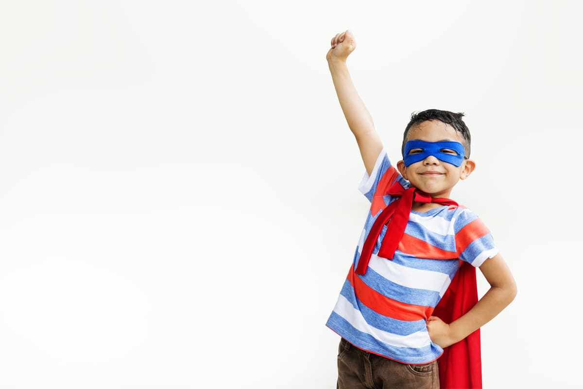 Criança com capa e bandana de super-herói e braço erguido em pose