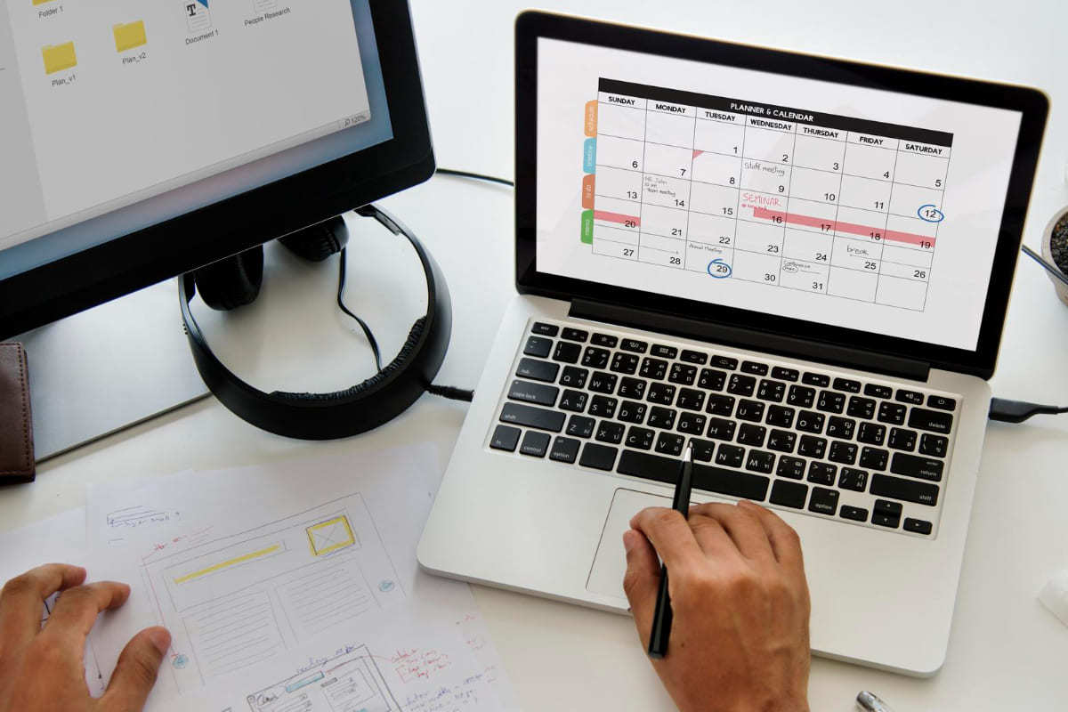 Dados: marketing sazonal Homem usando notebook sobre mesa branca com monitor grande à sua esquerda analisando dados em folha impressa