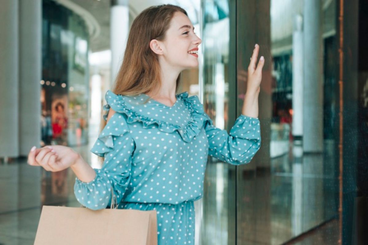 Mulher de azul usando bolsa de marca marrom e sorrindo empurrando porta de vidro