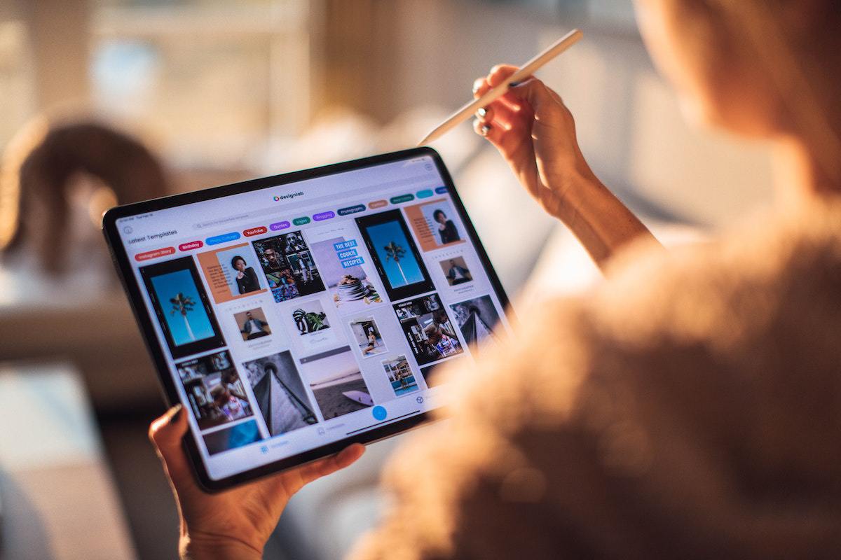 Pessoa segurando lápis de madeira e tablet com tela grande visualizando imagens no mesmo com objetos em desfoco ao fundo da foto