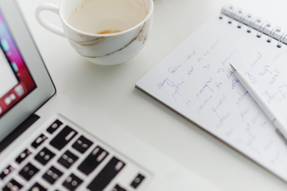 Notebook: Planejadores de palavra-chave Notebook branco sobre mesa de mesma cor ao lado de xícara e agenda aberta