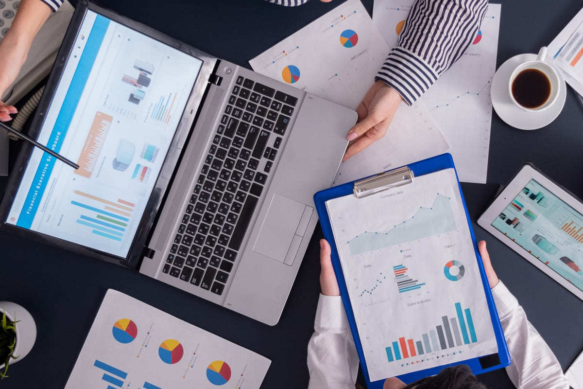 Pessoas sentadas ao redor de mesa de reunião enquanto analisam dados em notebook e tablets