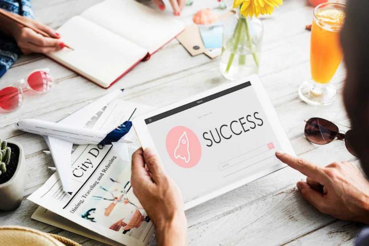 Pessoa segurando tablet branco com montagem na tela com foguete e mostrando palavra SUCCESS com alguns objetos espalhados na mesa
