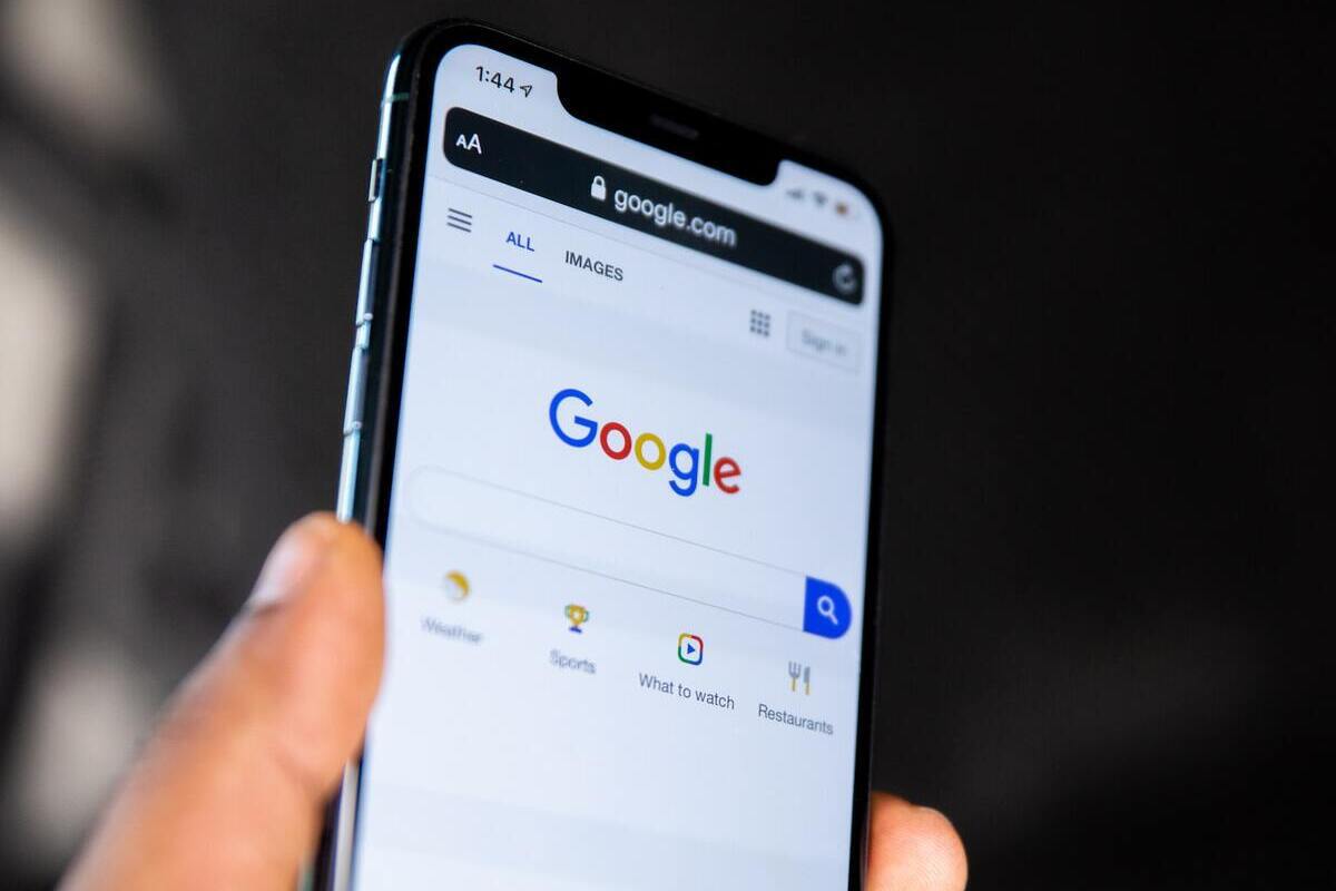 Pesquisa Google: Saturação de palavras-chave Pessoa segurando celular na mão que está com navegador aberto em tela inicial de pesquisa Google