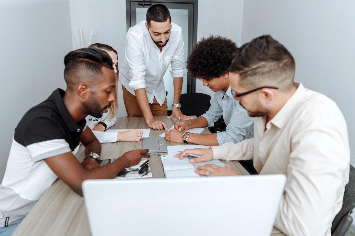 Reunião: smarketing Homens e mulher sentados ao redor de mesa de madeira e outro homem de pé enquanto analisam dados de empresa