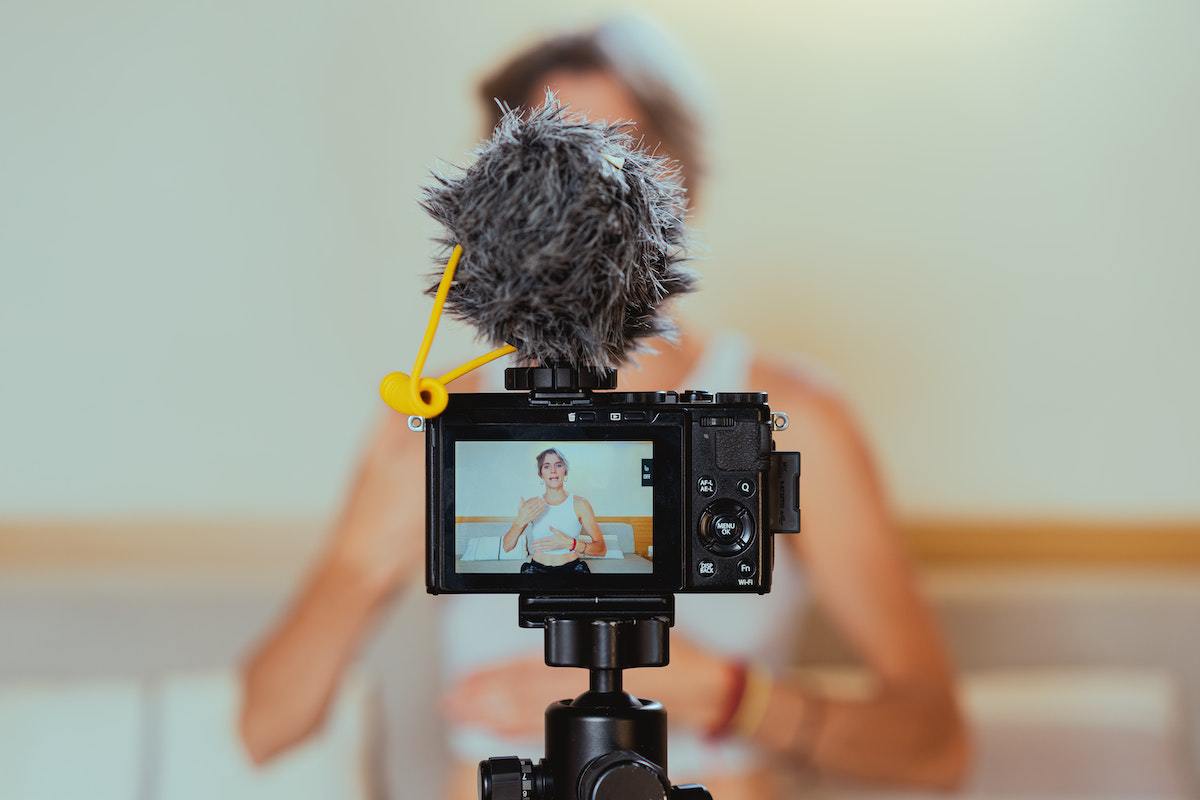 Gravação: Tipos de vídeo Câmera sobre pedestal semi profissional com microfone acima acoplado filmando mulher gesticulando