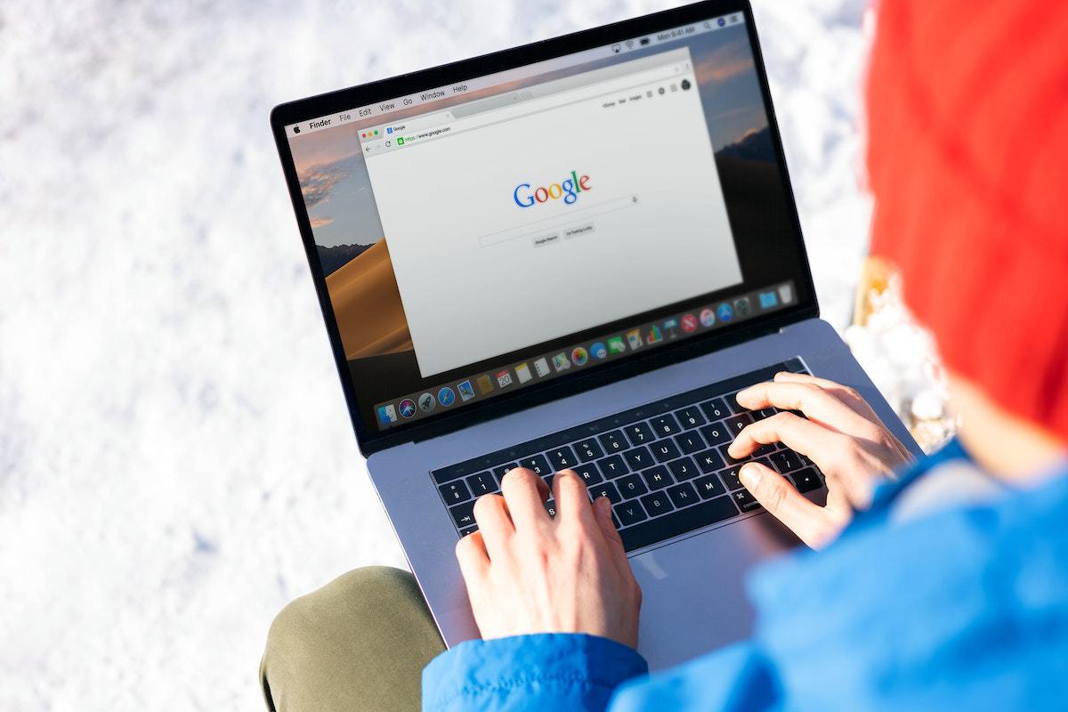 Pessoa sentada com pés na neve e segurando notebook no colo enquanto usa o mesmo para pesquisar na home do Google