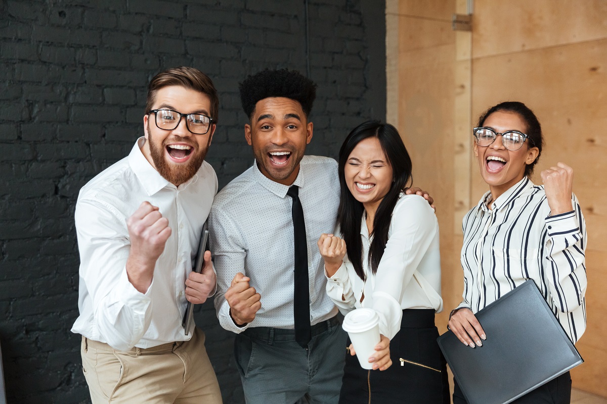 Dois homens e duas mulheres sorridentes e comemorando algo lado a lado em local de trabalho com roupa social