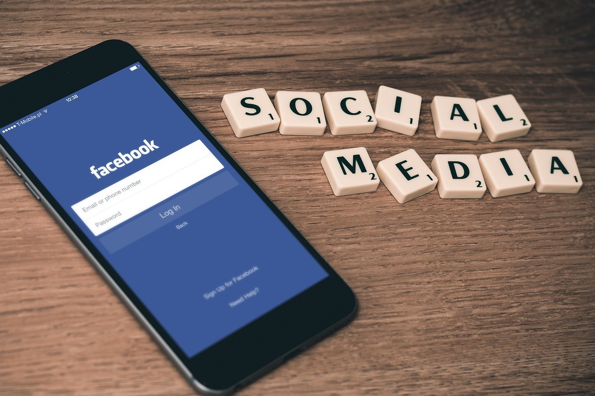 Celular: turbine suas vendas Celular sobre mesa aberto em tela de login do Facebook ao lado de peças de jogo palavras cruzadas formando frase Social Media