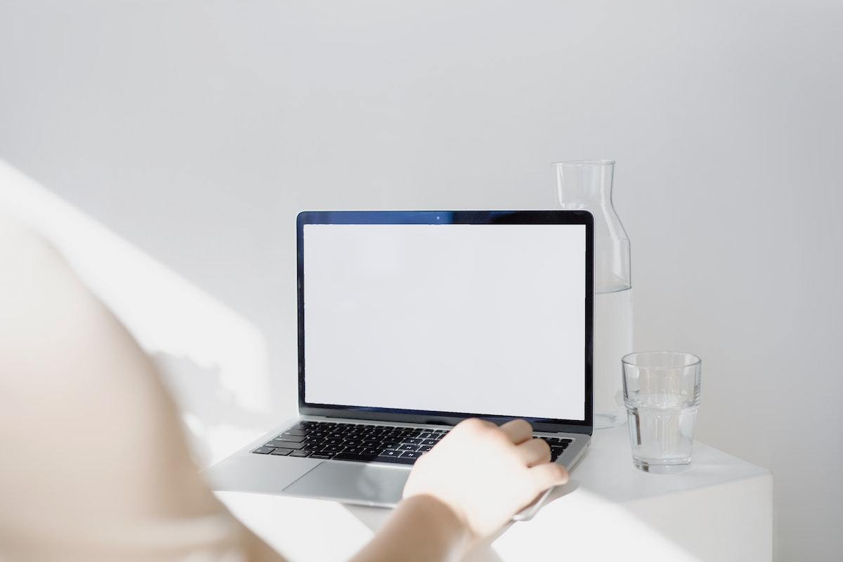 Mulher usando notebook cinza sobre mesa branca com copo de vidro ao lado