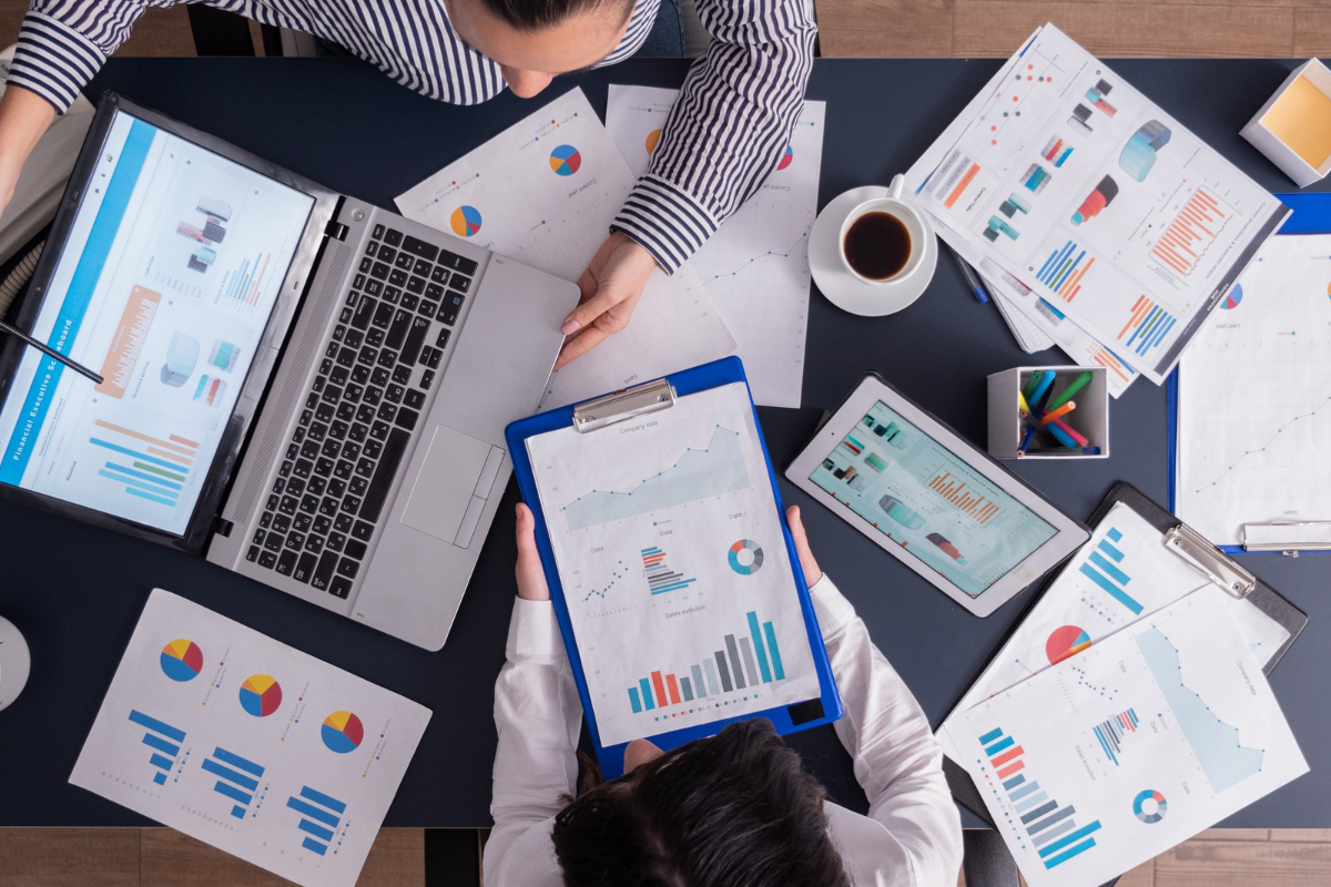 Análise de dados: verdades sobre SEO Pessoas sentadas diante de mesa, uma em cada lado, analisando dados em folhas e notebook