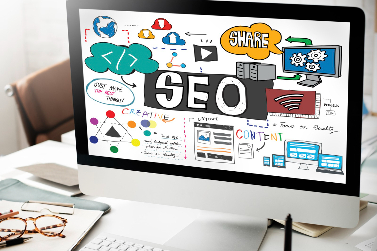 Computador: verdades sobre SEO Computador de mesa branco sobre mesa de mesma cor com montagem na tela com símbolos sobre SEO