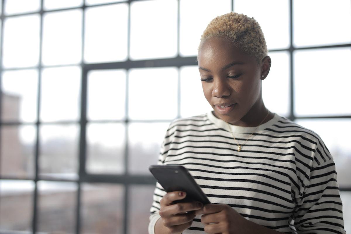 Mulher usando celular diante de grandes janelas de vidro de edifício