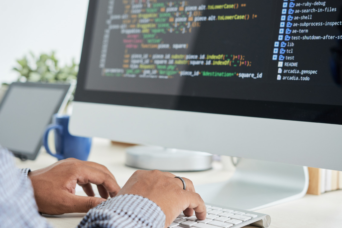 Pessoa programando em computador branco em cima de mesa branca de escritório