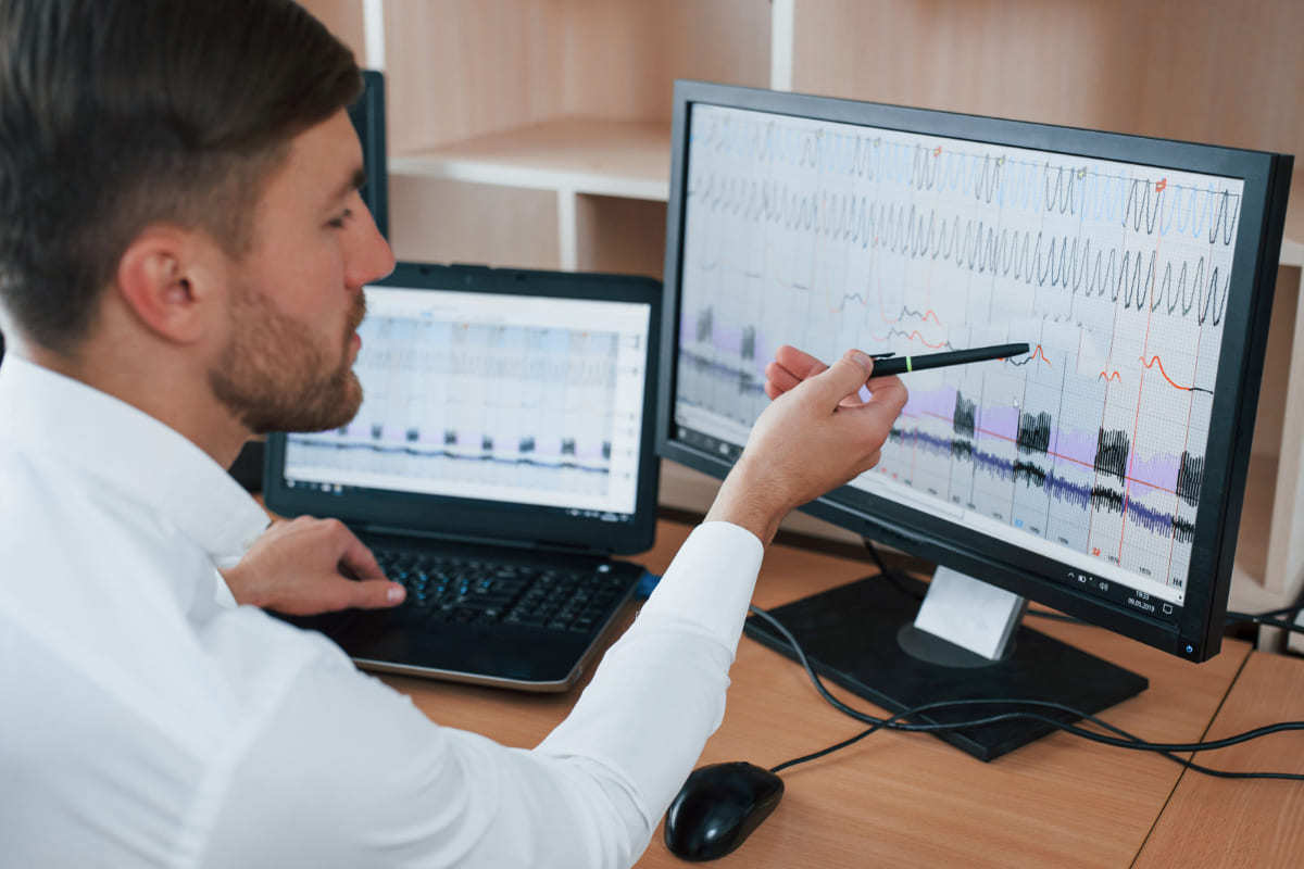 homem analisando gráficos: análise preditiva homem analisando gráficos em dois computadores