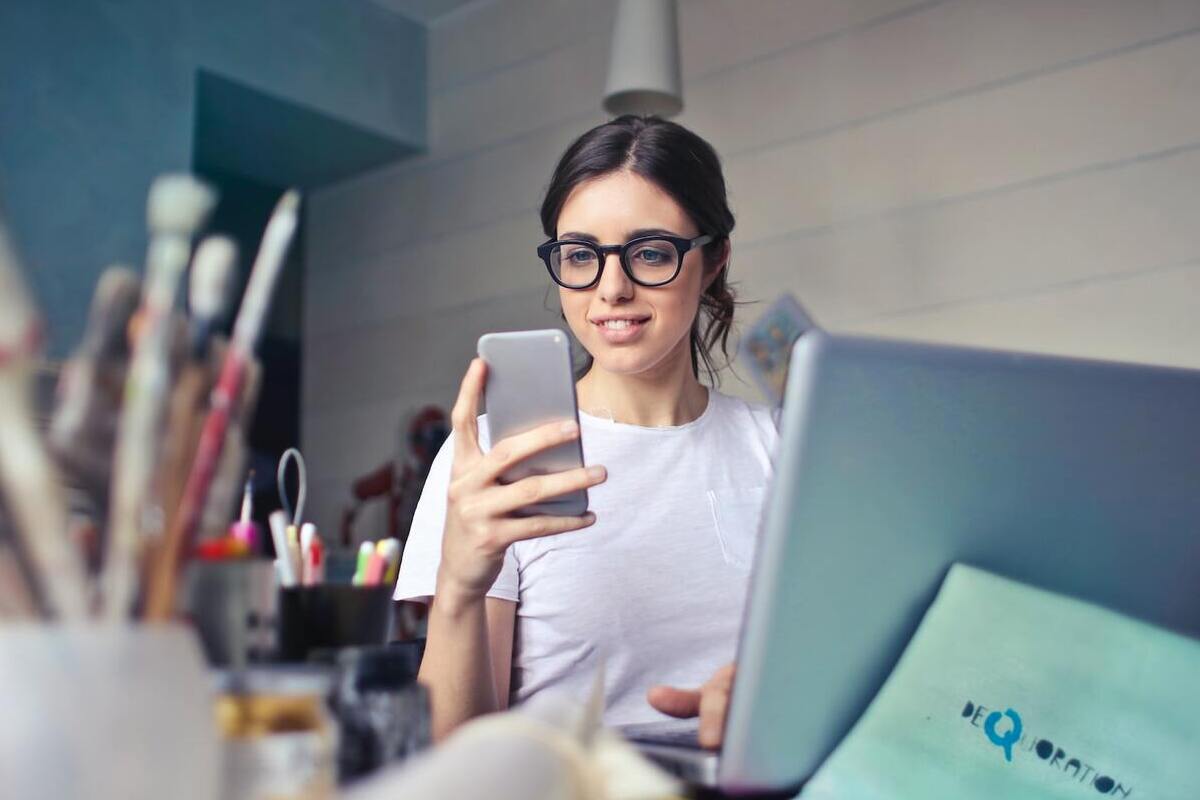 mulher usando celular e laptop: aplicativos para criar vídeos mulher sentada, usando laptop e celular ao mesmo tempo