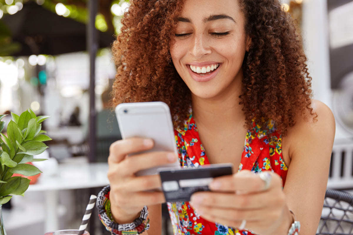 compras online: atribuição multicanal mulher usando um celular e segurando um cartão de crédito