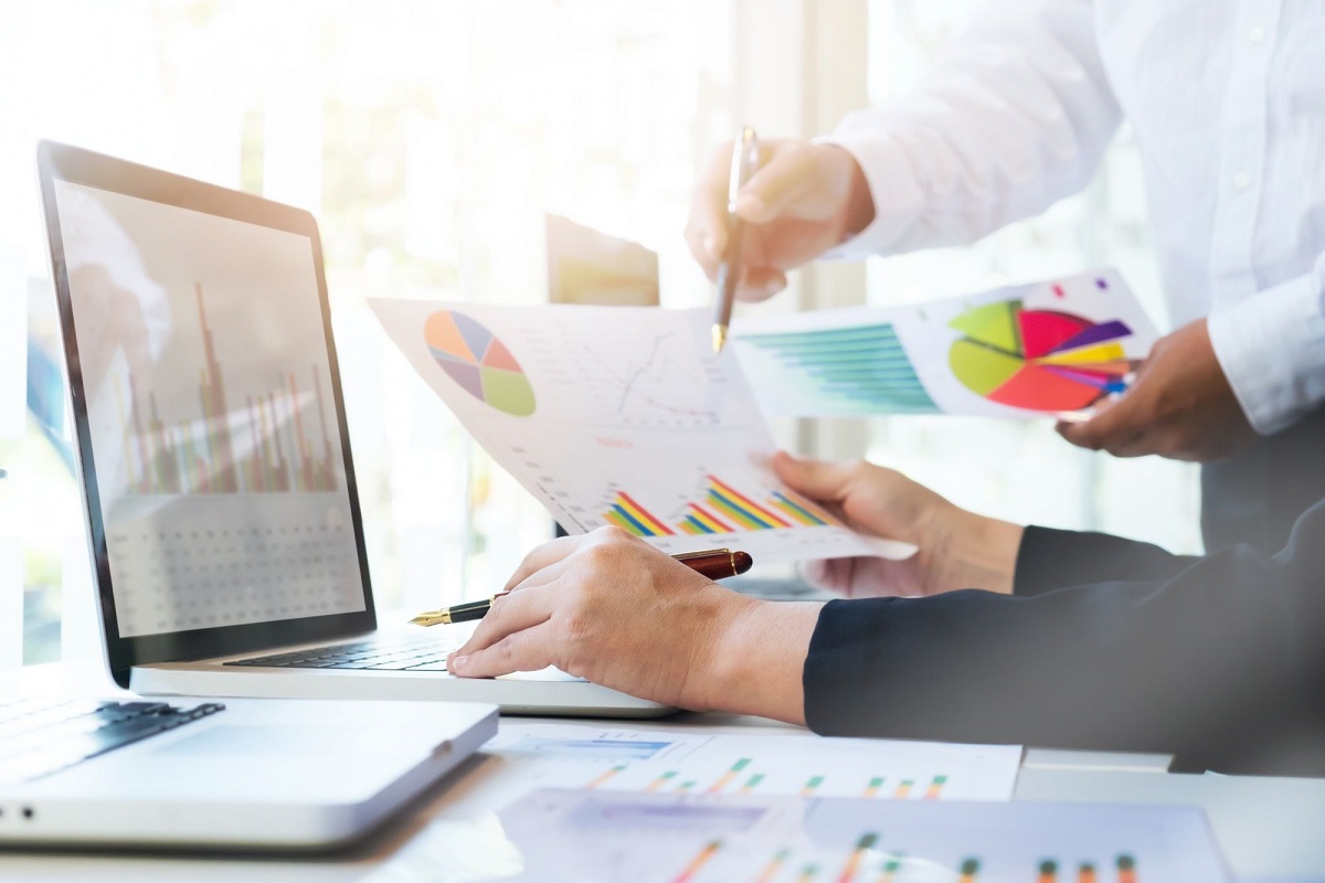 Pessoa checando dados: Autocomplete e pesquisas relacionadas. Autocomplete e pesquisas relacionadas: A imagem mostra uma pessoa com algumas folhas de dados impressos ao seu redor enquanto confere cada um no computador.