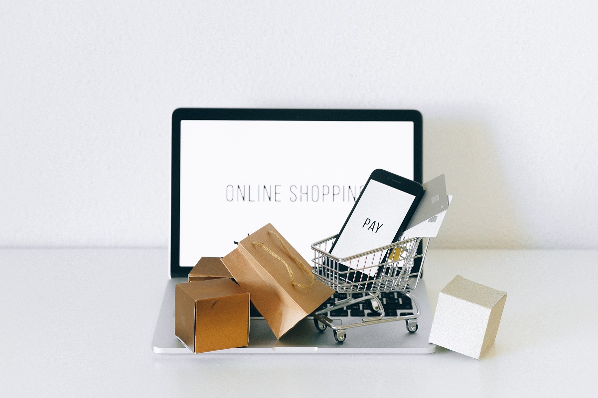 Branding para e-commerce: A imagem mostra um computador e por cima dele algumas sacolas de compras, carrinhos de compra e máquina de cartão. 