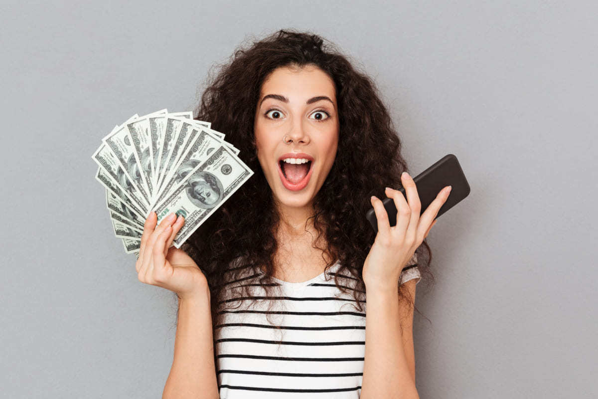 mulher segurando celular e dinheiro: como monetizar aplicativo mulher com dinheiro em uma mão e o celular em outra