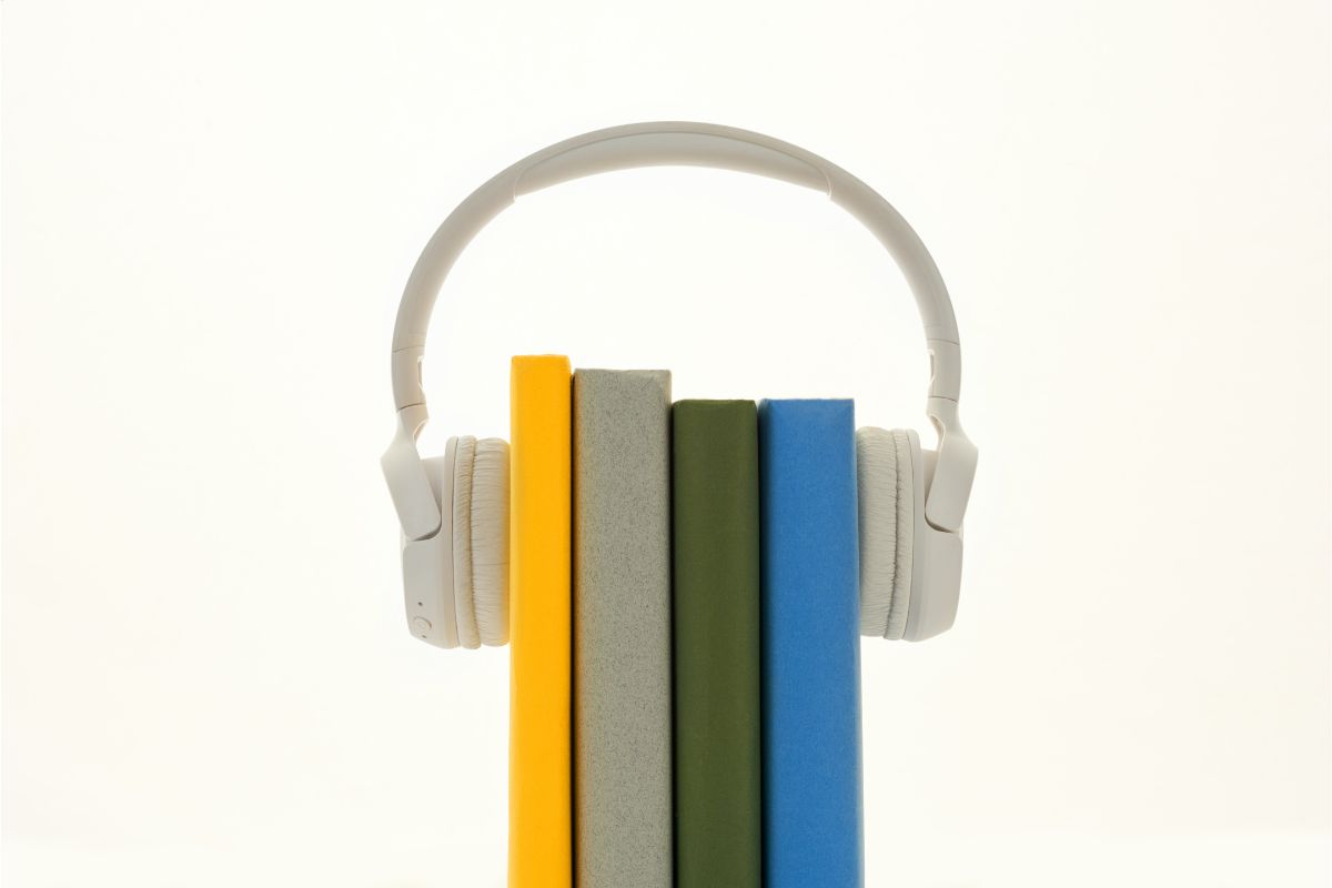 Conteúdo em áudio: a imagem mostra alguns livros e sobre eles um fone de ouvido. 