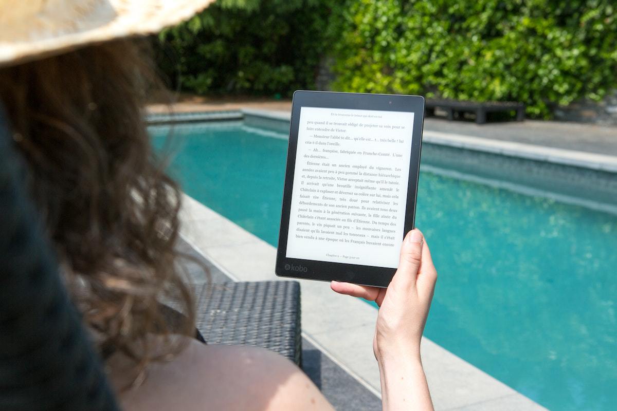 mulher sentada de frente para a piscina, lendo no kindle