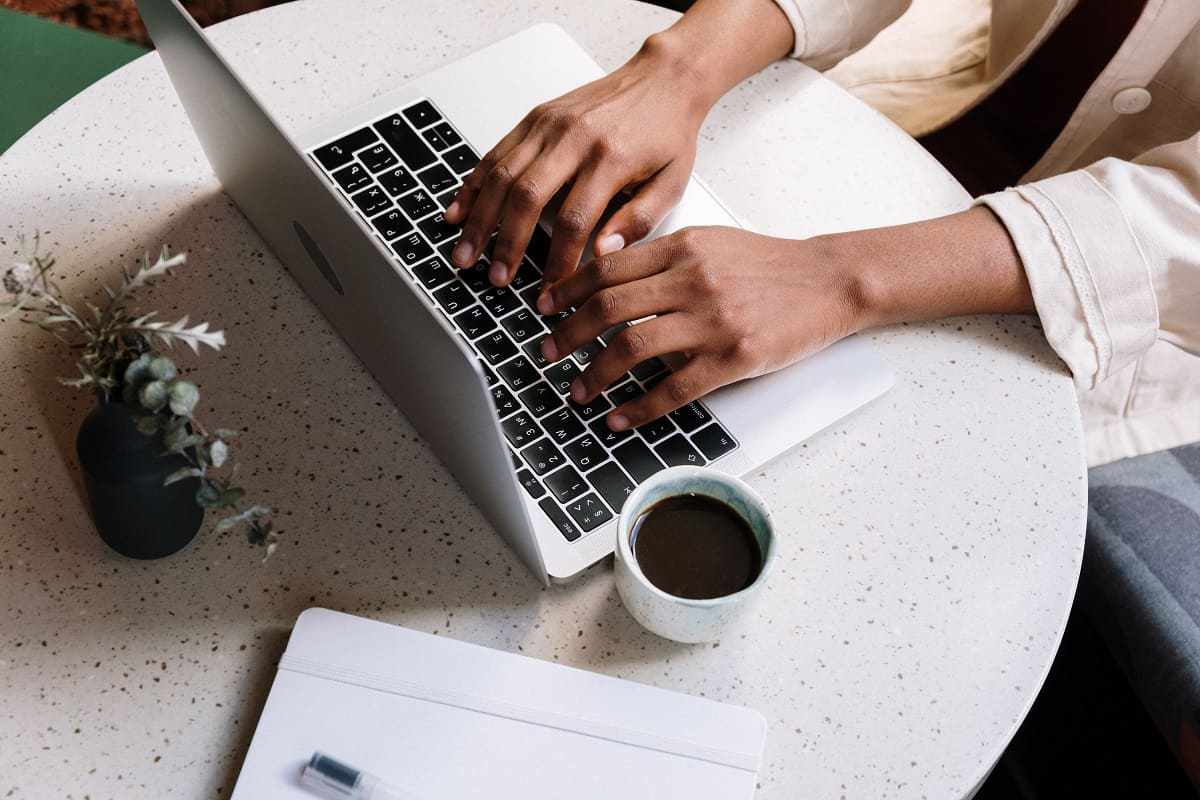 pessoa trabalhando em seu laptop com uma xícara de café do lado