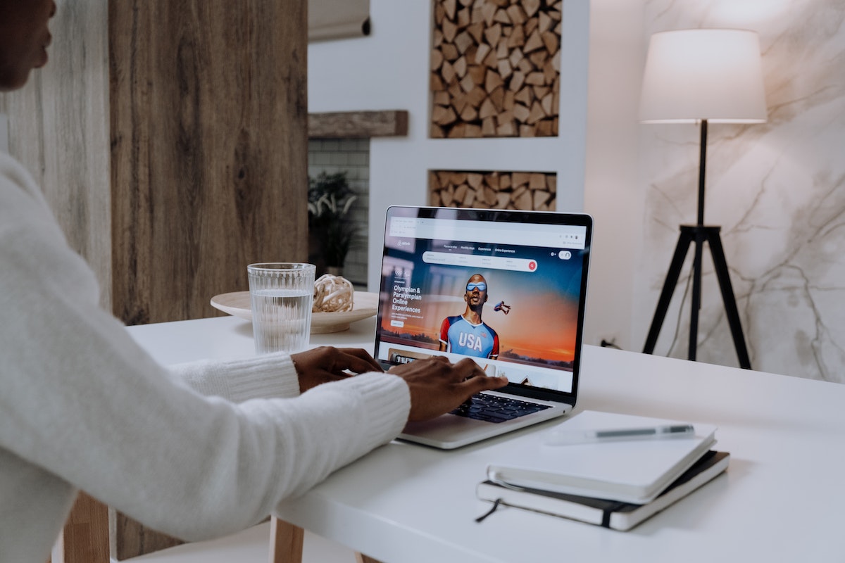 pessoa usando laptop para trabalhar e, ao seu lado, há um copo de água e dois cadernos