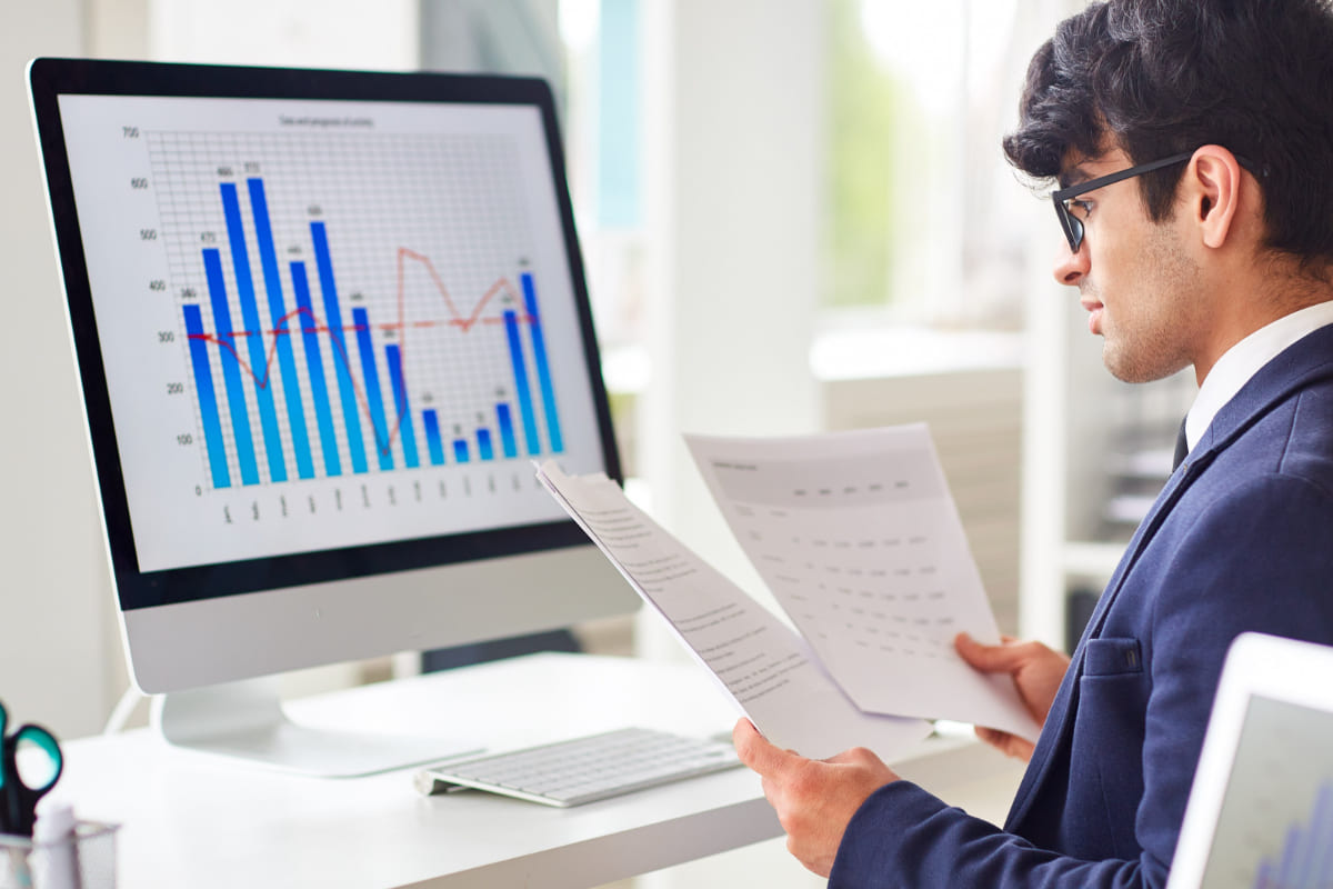 análise de relatórios: analista de seo homem de frente para um desktop analisando folhas de relatórios